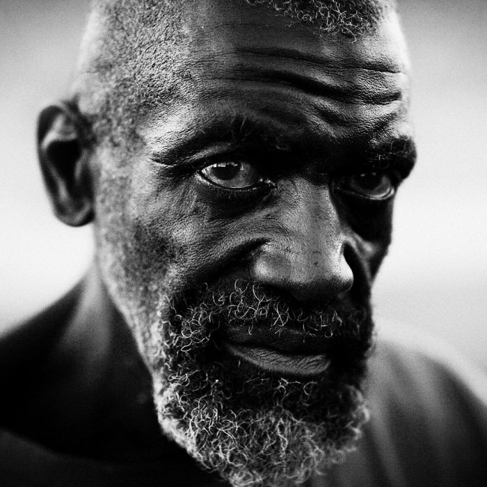 Monochrome side profile portrait of an elderly man with a grey beard looking sideways into a sharp light source.