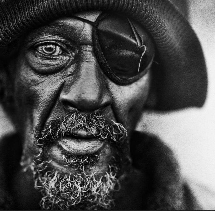 Gritty asymmetrical black and white portrait of an expressive man with strong textural shadows.
