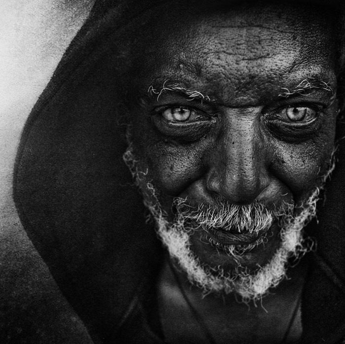 High contrast black and white portrait of an old man wearing a coarse winter jacket hood covering his head.