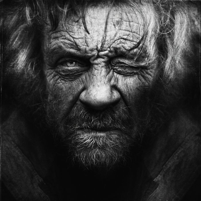 Brutalist low key black and white portrait of a man with rough beard emerging from pure dark shadows.