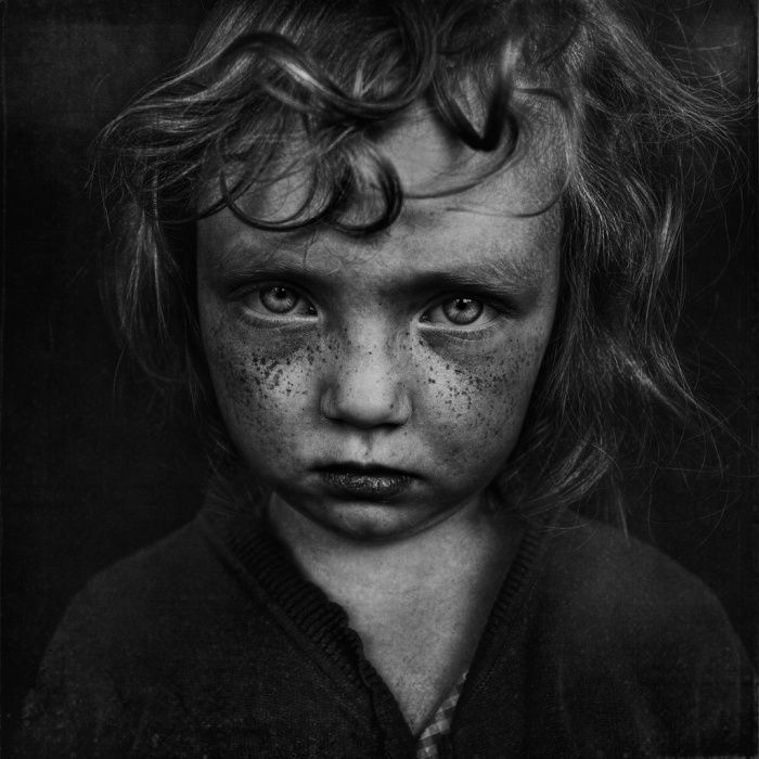 Haunting close up black and white portrait of a young child with intense dramatic eyes and texture framing.