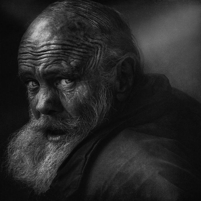 Haunting black and white close up photo of an old man with closed eyes and detailed grey beard texture.