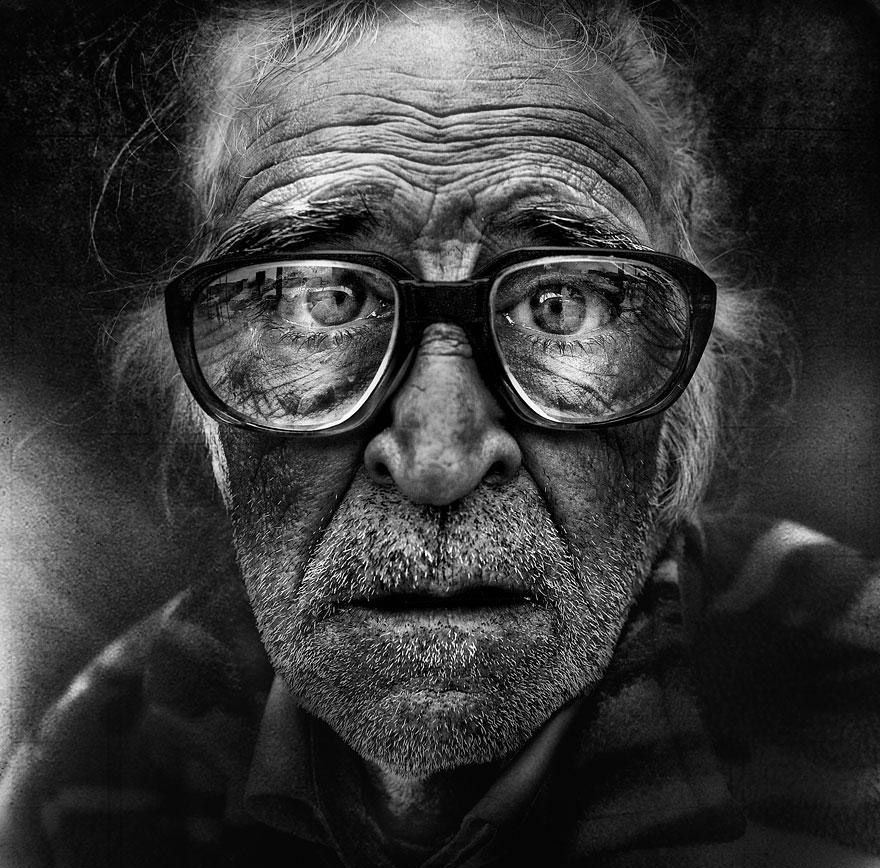 Gritty high contrast black and white portrait of an old homeless man with glasses by Lee Jeffries highlighting extreme facial wrinkles.