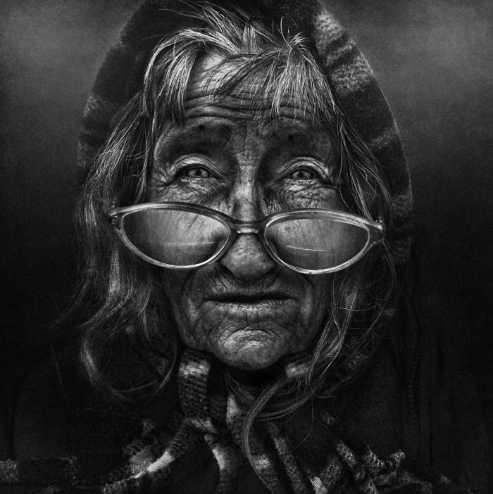 Atmospheric black and white portrait of an old man with glasses and detailed clothing texture under low key studio lights.