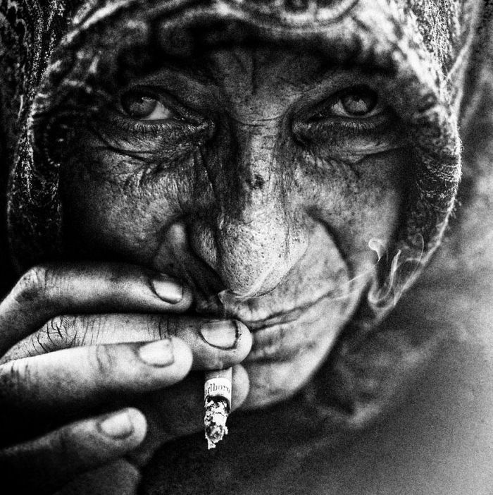 Grayscale close up conceptual portrait of an old homeless person holding a cigarette near their mouth.